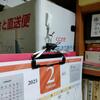 机の前のダンボール箱にピンフックをさして、カレンダーを引っかける