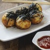 タコ焼き（日本のシーフード７）　Tasteatlas「世界のシーフード」ランキングの第87位．　タコ焼きやお好み焼きは，洗練された日本料理ではありませんが，アメリカでは「鉄板で焼くライブ感や分け合うことがシャア文化にあう，マヨネーズやソースの濃厚さ，等が気に入られ「面白くて濃厚な日本のファストフード」として人気．一方，フランスではガレットやクレープの延長線上の食べ物と受け取られていて，洗練さはないものの，家庭的で楽しい料理と受け止められているようです（ChatGPTまとめ）．