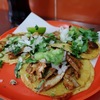 タコス・アル・パストール１（北米の肉料理7）　メキシコ料理に欠かせないユニークな料理．回転する串に刺した薄くスライスした豚肉をトルティーヤに載せ，玉ねぎ，刻んだコリアンダー，パイナップルの角切り，チリ，サルサをトッピングします．起源は，20 世紀初頭にメキシコに料理の伝統を持ち込んだレバノン人移民たちにさかのぼります．彼らの独自のシャワルマ調理技術が現地の食材に取り入れられ，一方，スパイスは変更され，ラム肉は豚肉に置き換えられました．